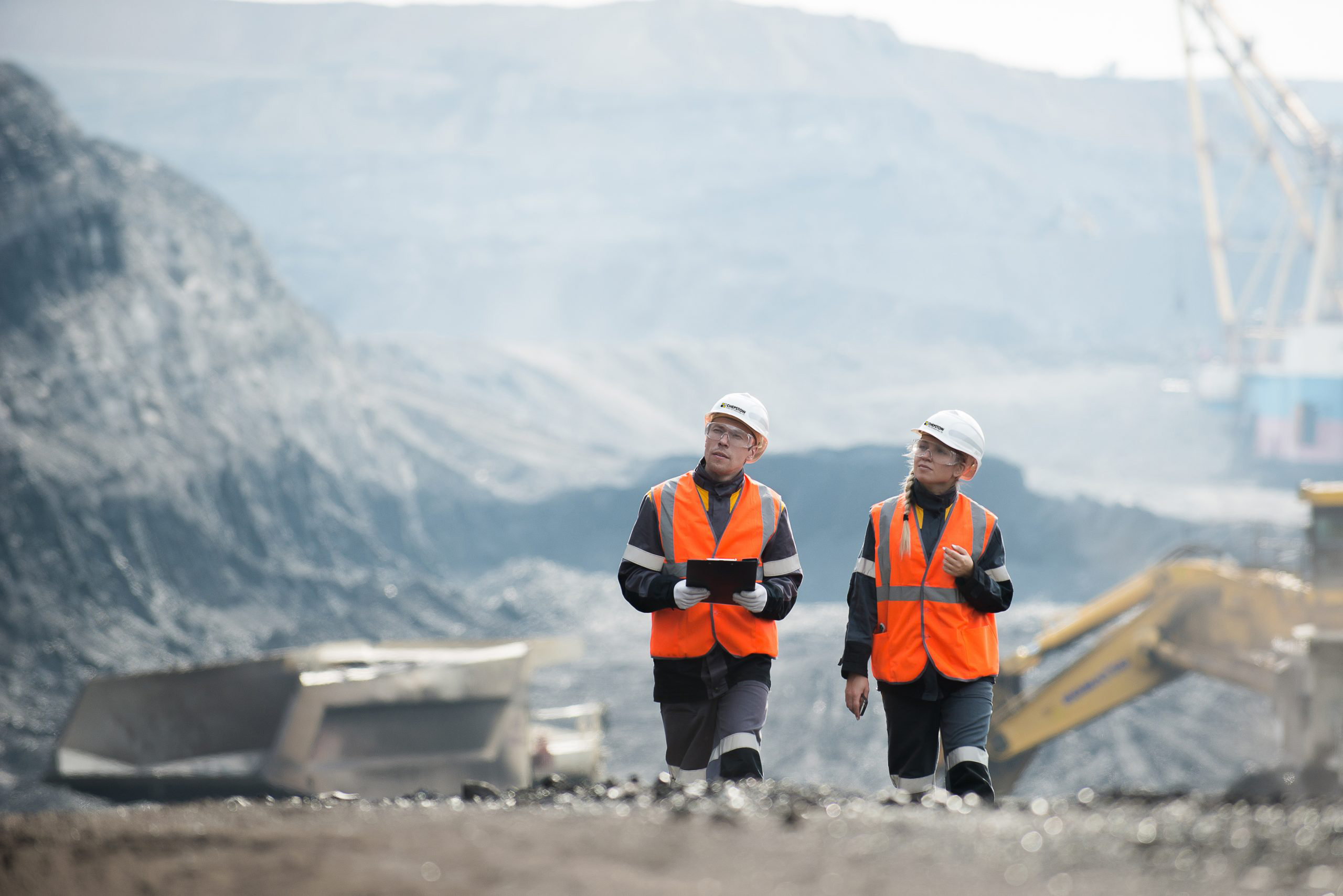 two people walking through quarry with Chepstow Plant helmets on